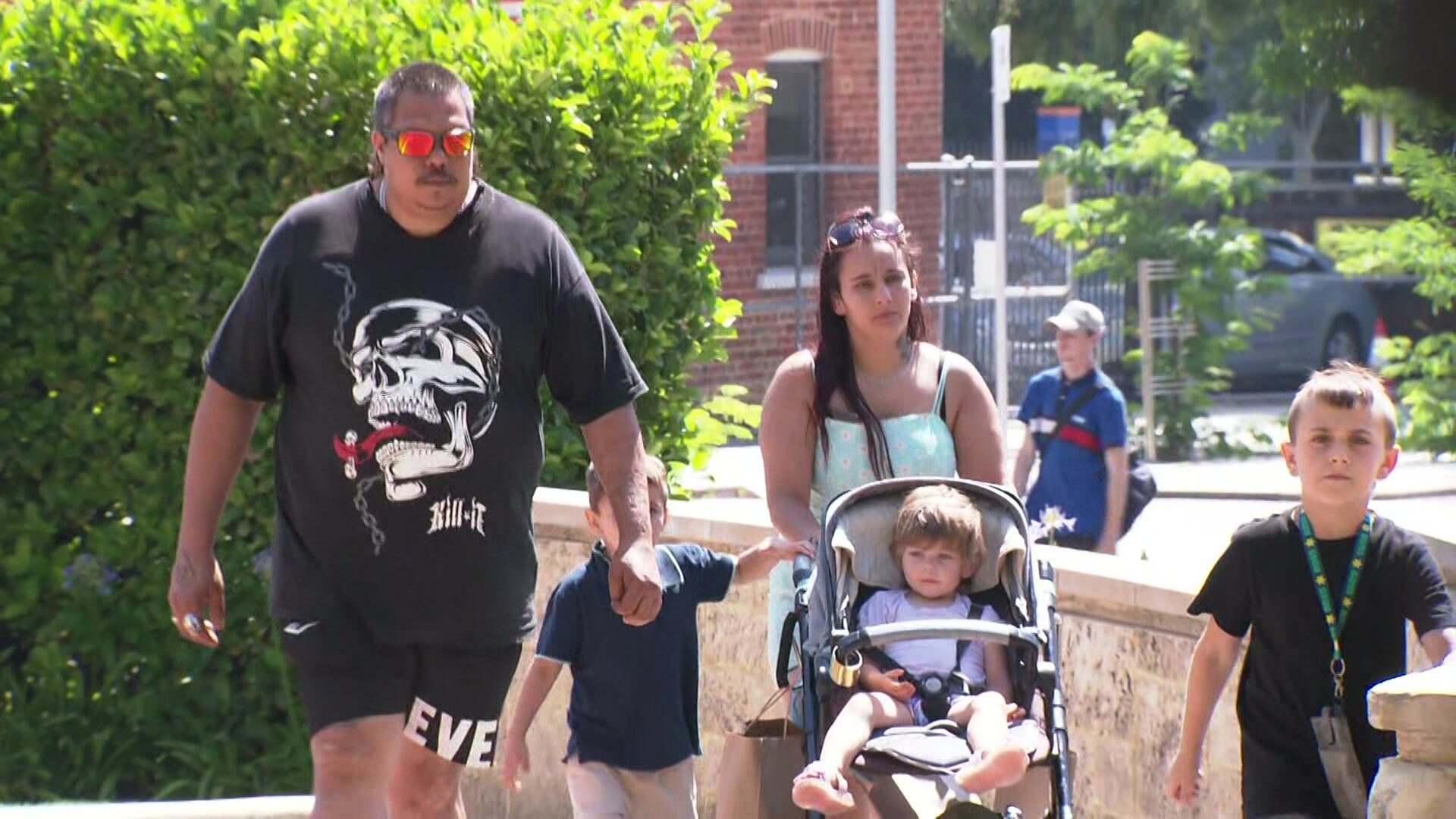 A male and female walk with a young child and a pram