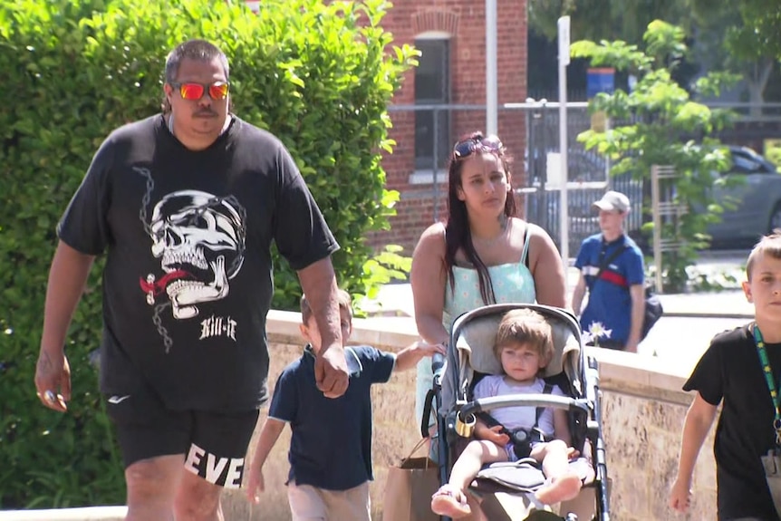 A male and female walk with a young child and a pram