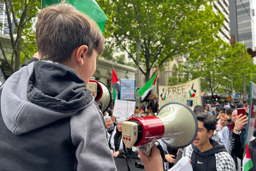 A child sits on an adult's shoulders holding a megaphone at a rally. 