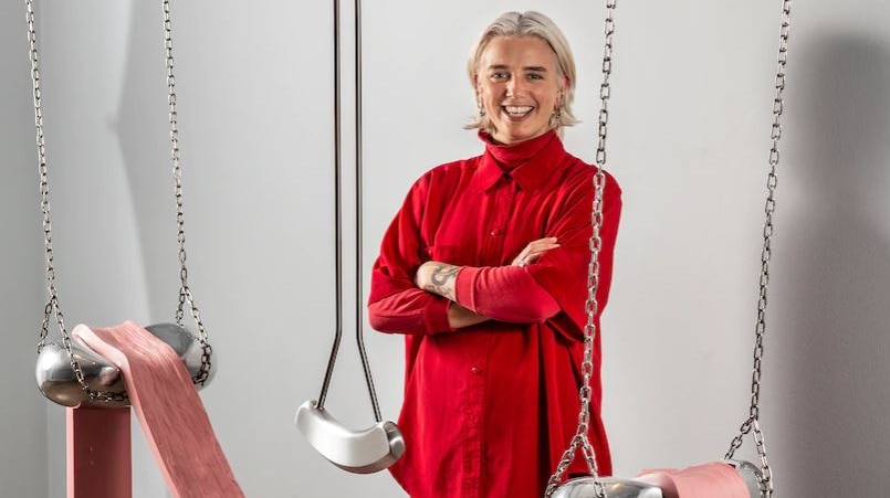 A woman in red standing next to a large pendulum artwork