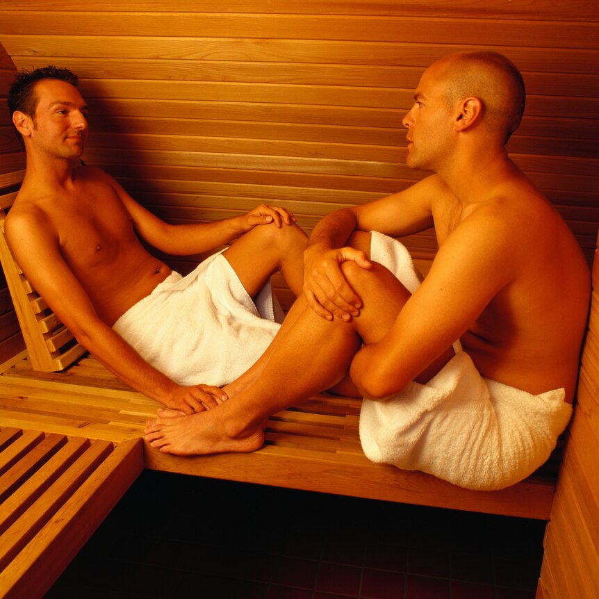 Two men wearing towels sitting in a sauna facing each other