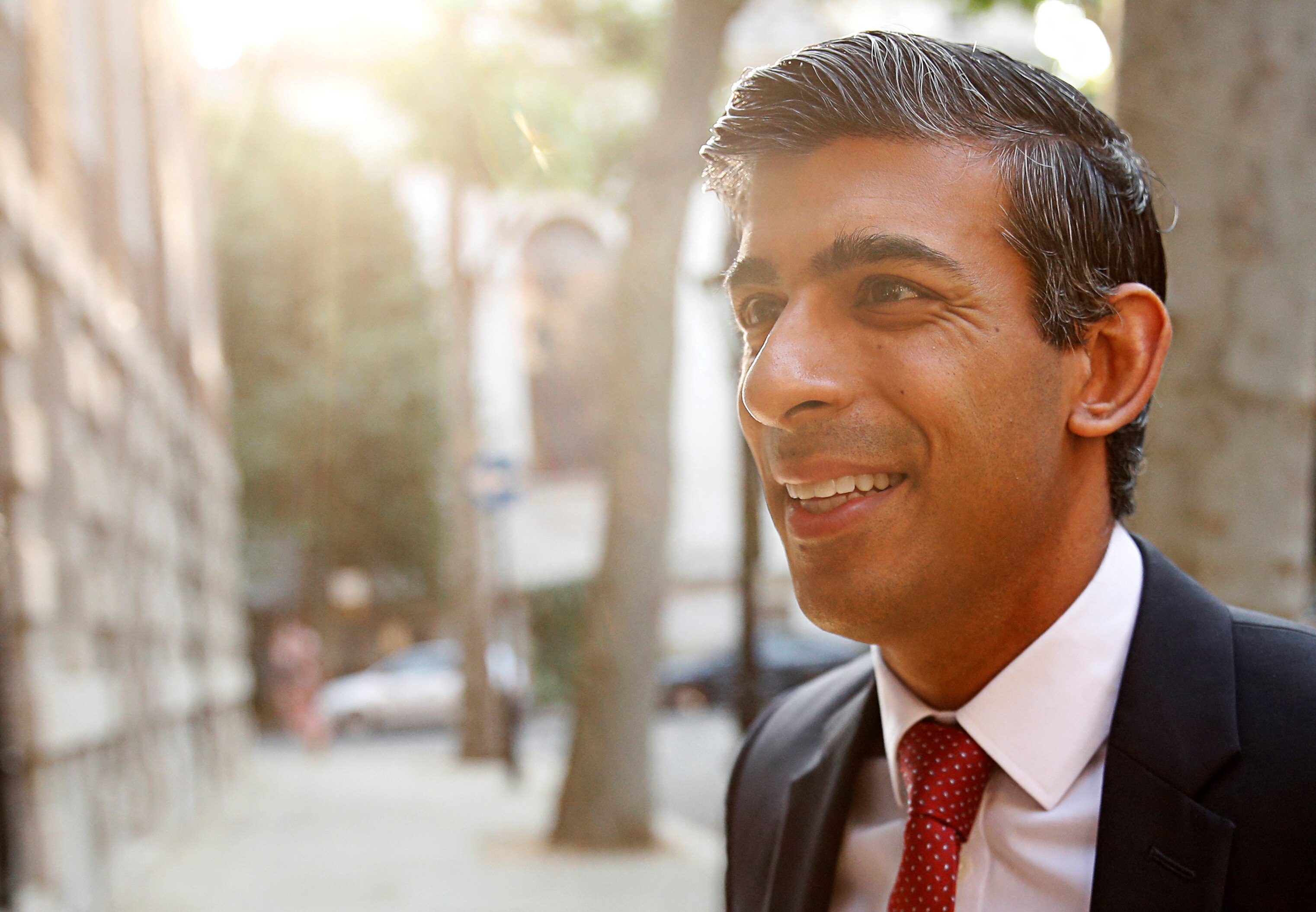 Ο Rishi Sunak χαμογελά καθώς ο ήλιος λάμπει στο πρόσωπό του