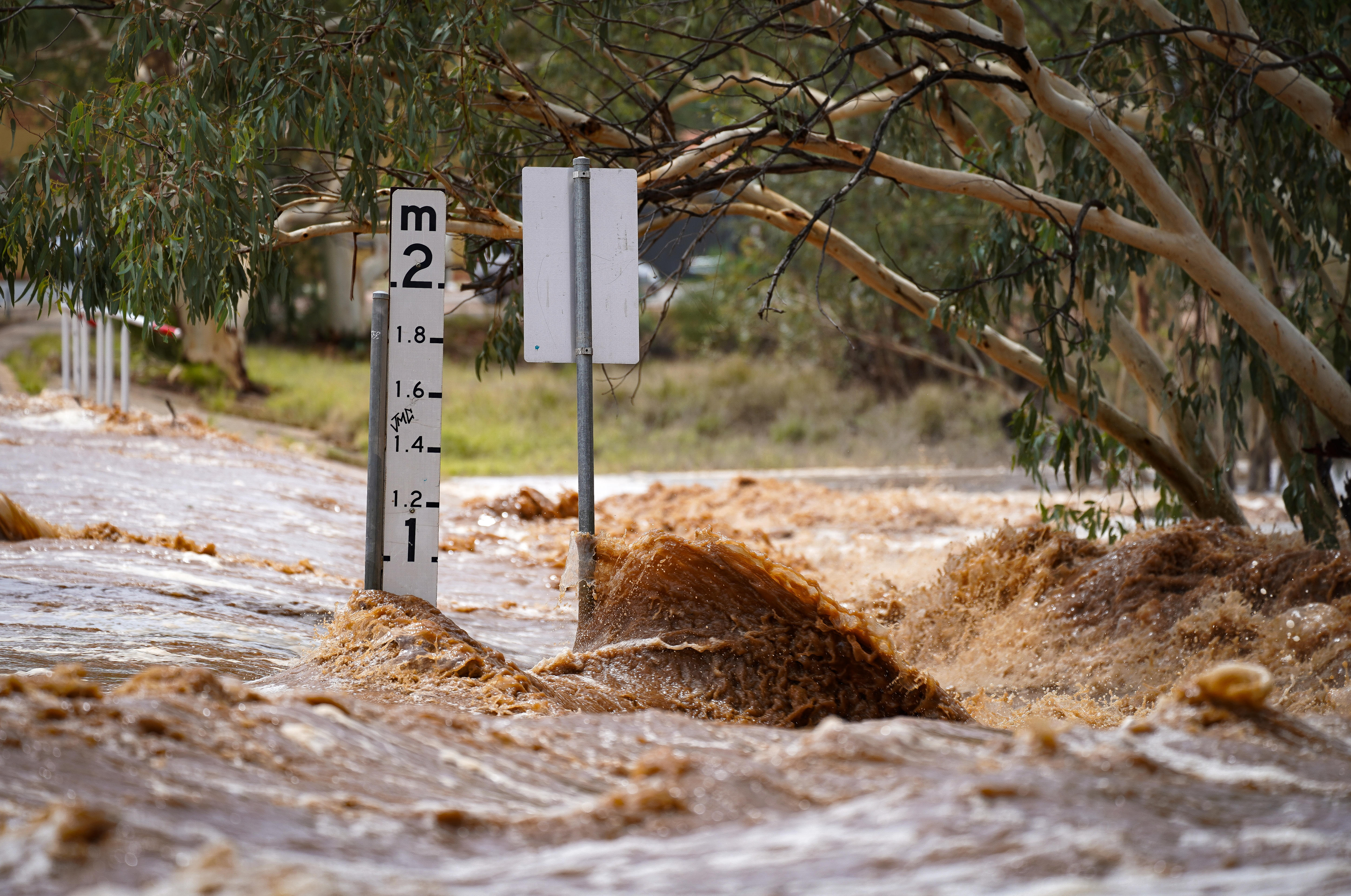 Olas de agua de inundación chocan contra un cartel de indicador de inundación.