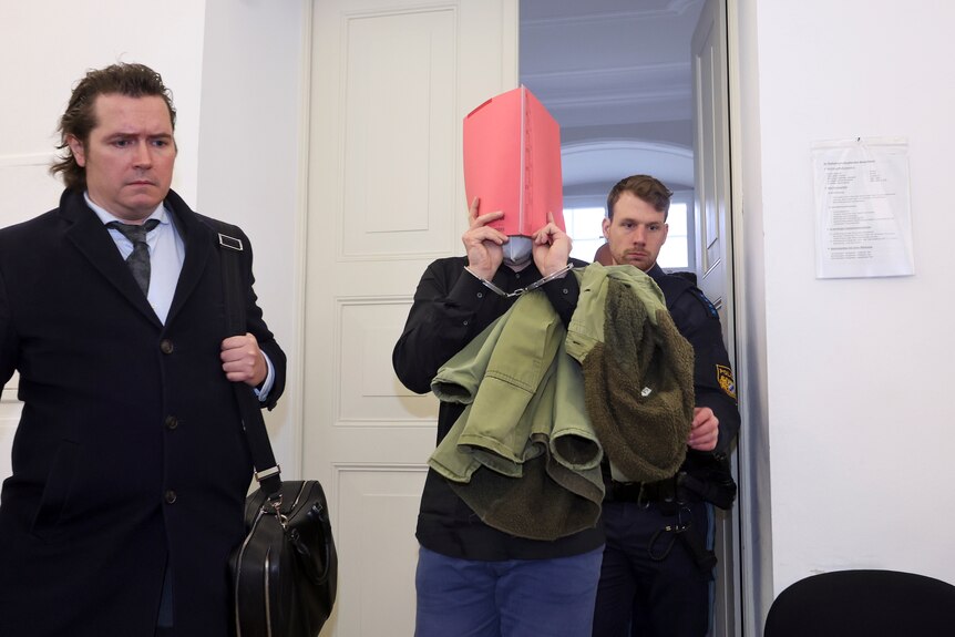 A 31-year-old American man accused of murder, center, is led into the courtroom at the regional court in Kempten, Germany. 