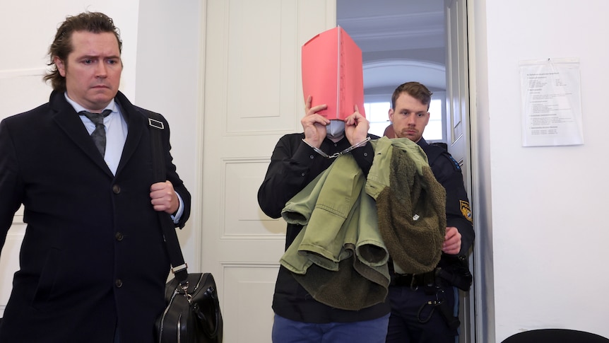 A 31-year-old American man accused of murder, center, is led into the courtroom at the regional court in Kempten, Germany. 