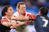 A St George Illawarra NRLW player holds the ball as she is tackled by a Sydney Roosters opponent.