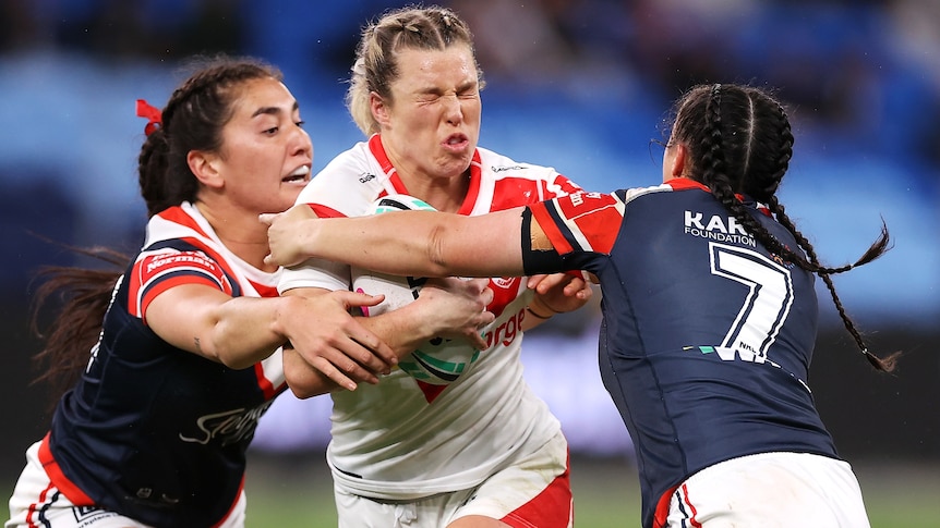 A St George Illawarra NRLW player holds the ball as she is tackled by a Sydney Roosters opponent.