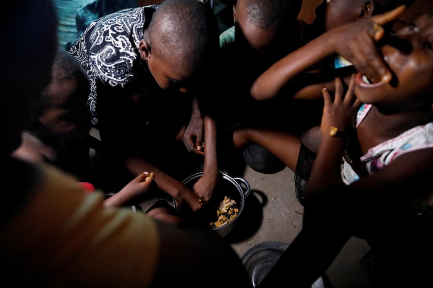 Young Nigerian children eat food out of a small metal pan with their hands.