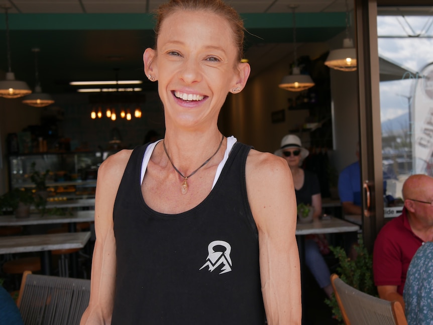 A woman stands smiling in front of her cafe with a crowd of people behind her.