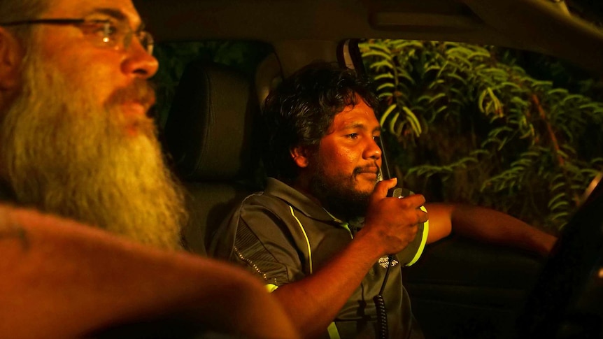 A photo of a Larrakia man sitting in a car, talking into a walkie talkie.