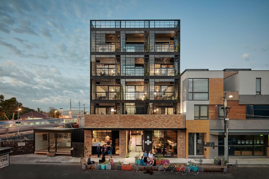 A five-floor apartment building with large glass windows and a shopfront on the bottom floor.