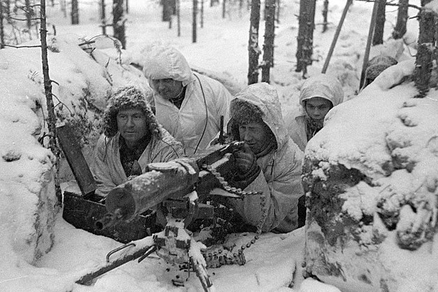 A group of men sit in a nest of Finnish machine guns in the snow.