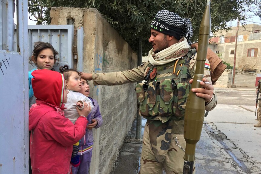 A soldier on the street holds a weapon and speaks to children recently liberated from Islamic State in Mosul, Iraq.