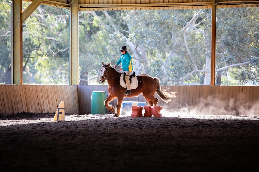 A man wears the Australian Olympic shirt while riding a brown horse