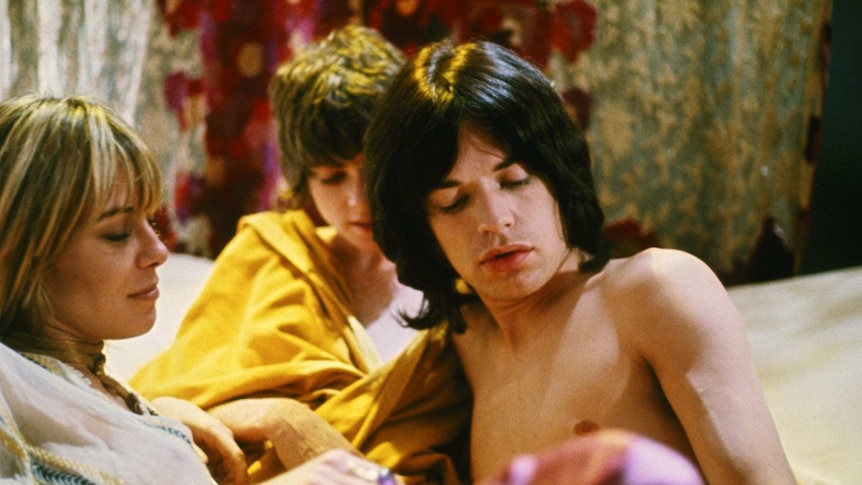Anita Pallenberg, Michele Breton and Mick Jagger lying together on a bed