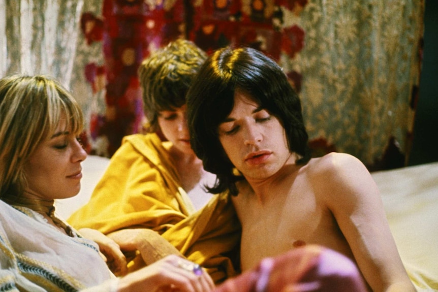 Anita Pallenberg, Michele Breton and Mick Jagger lying together on a bed