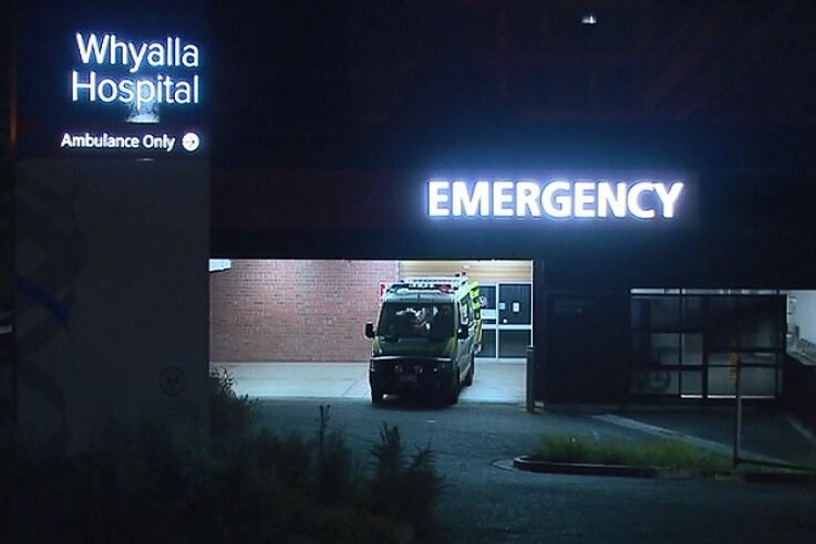An ambulance outside a hospital emergency driveway at night.