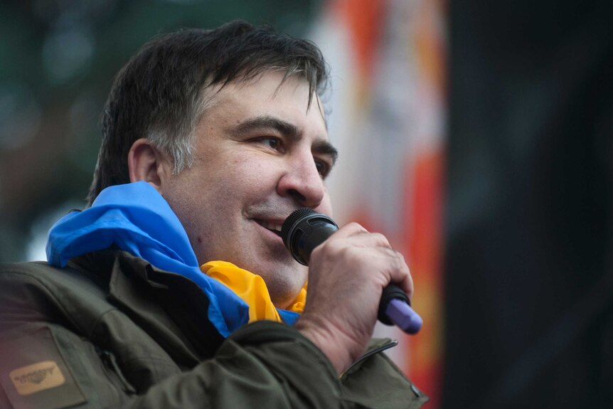 Close up view of Mikheil Saakashvili with a blue and yellow Ukranian flag around his neck and speaking into a microphone