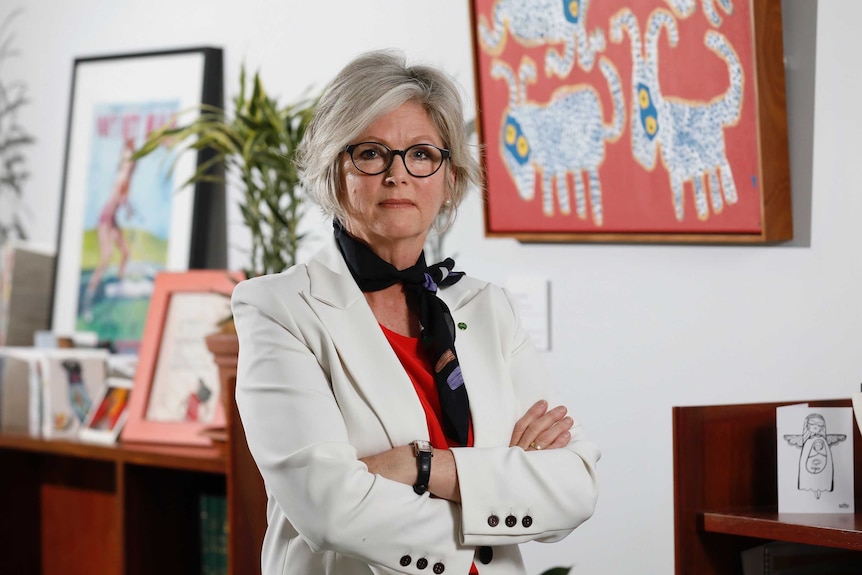 A woman looks stern and stands with her arms crossed in an office.