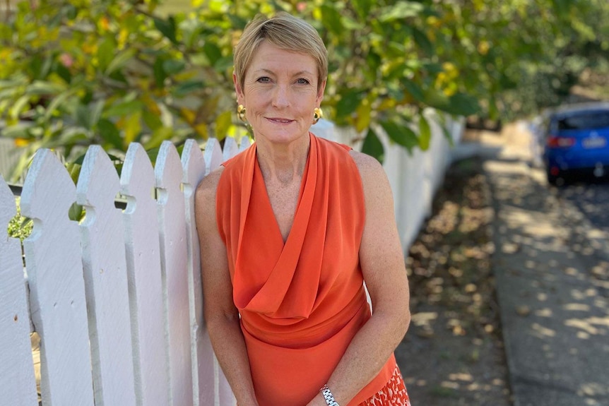 A woman smiles as she leans against a wooden picket fence