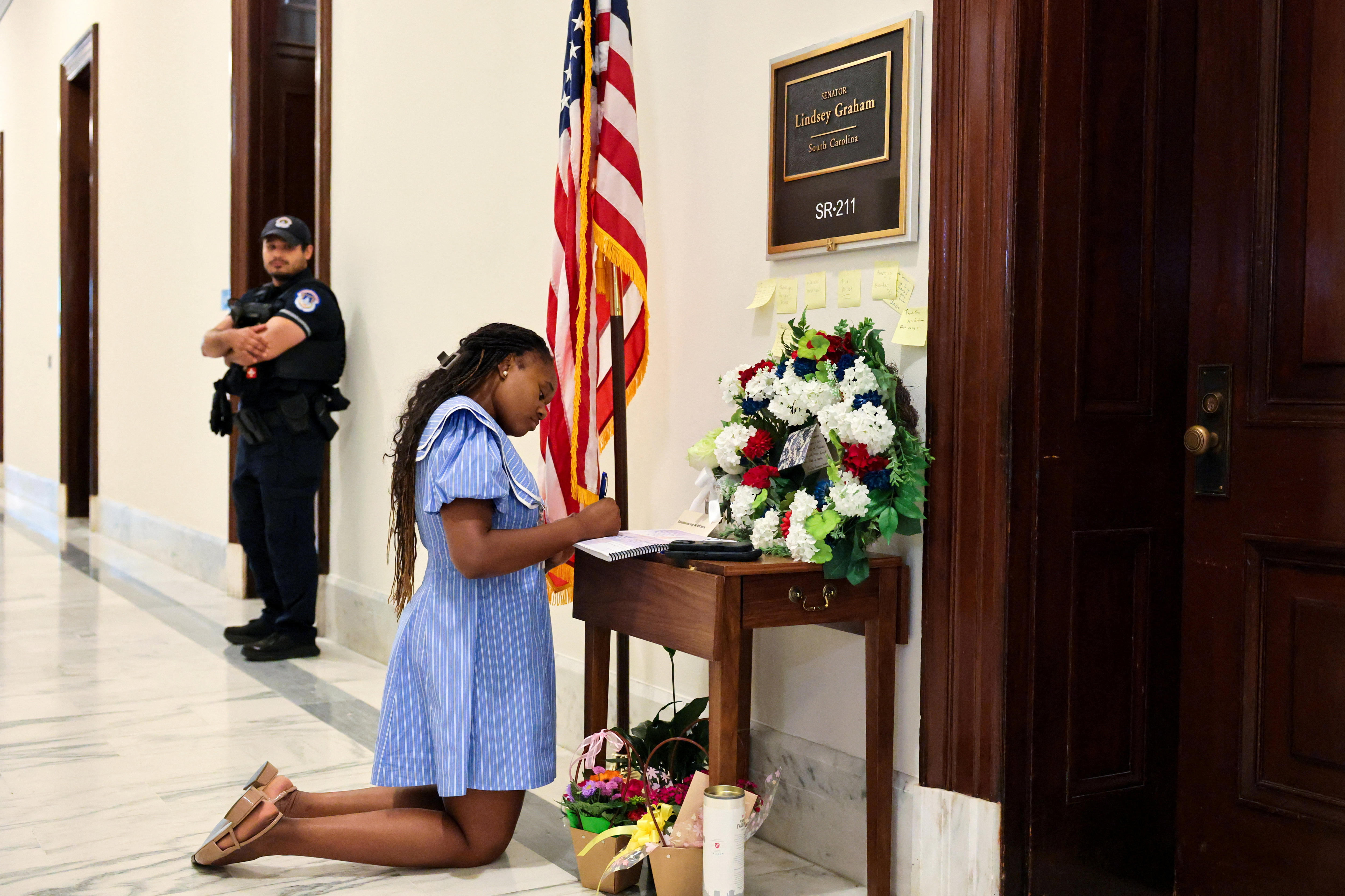 A woman kneels and writes in a book in a congressional building hallway.