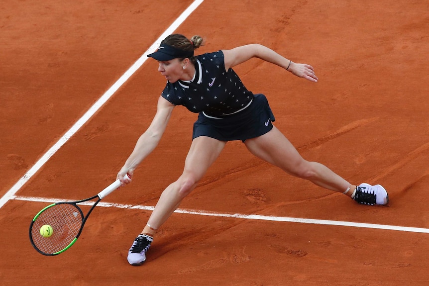 A female tennis player reaches down to get her racket to a ball on the claycourt.