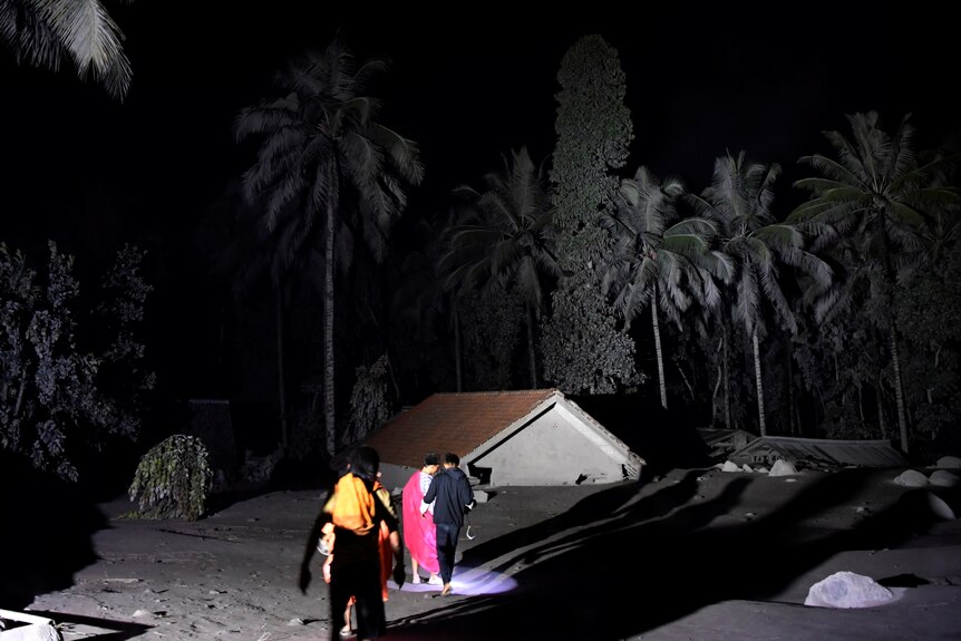 villagers can be seen walking near a house covered in grey volcanic ash at night