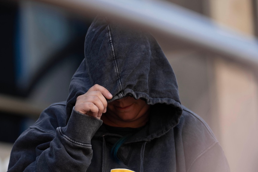Emma Weitnauer leaves court with her face covered by a hoodie.