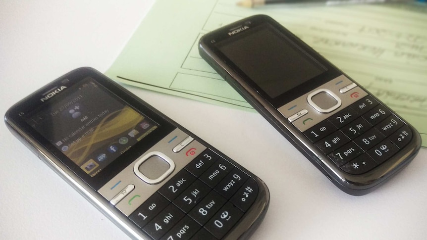 Two Nokia phones lie on a desk in front of a green form