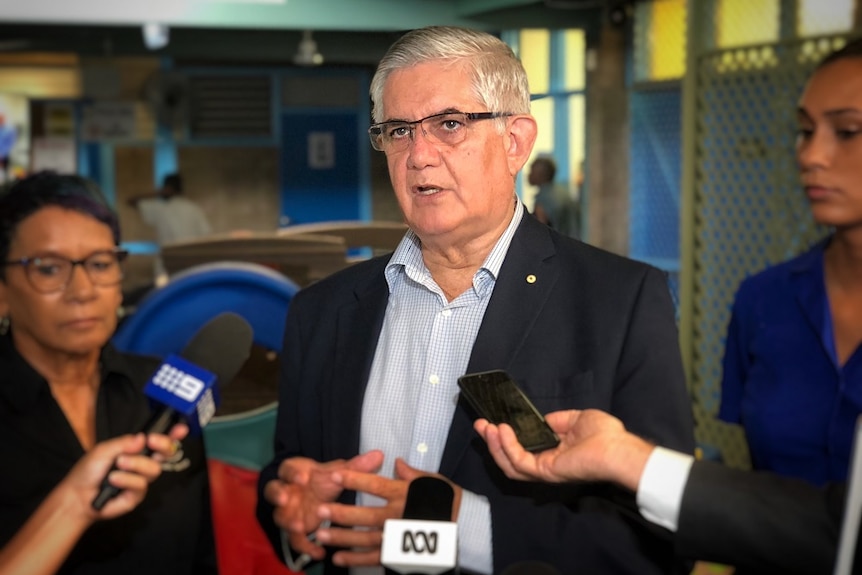 The minister speaks at a press conference, surrounded by the media.