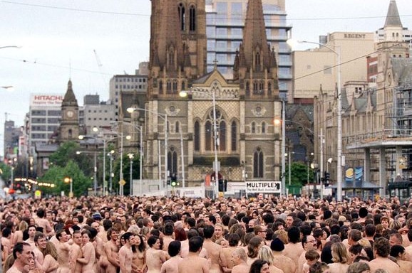 Sejumlah orang tak memakai baju berada di lapangan dengan latar belakang gereja di Melbourne.