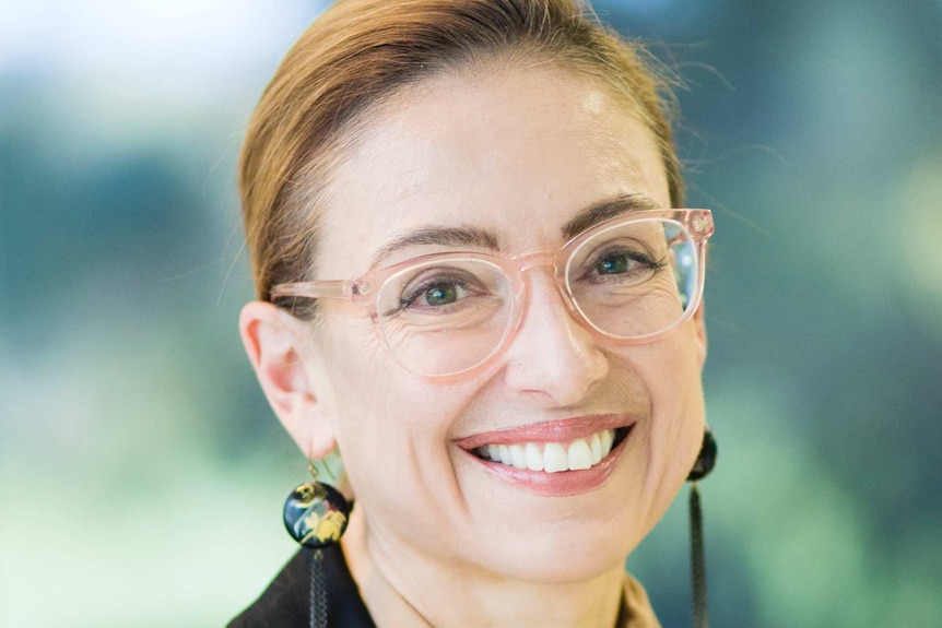 A headshot of a woman wearing glasses, blouse and a vest.