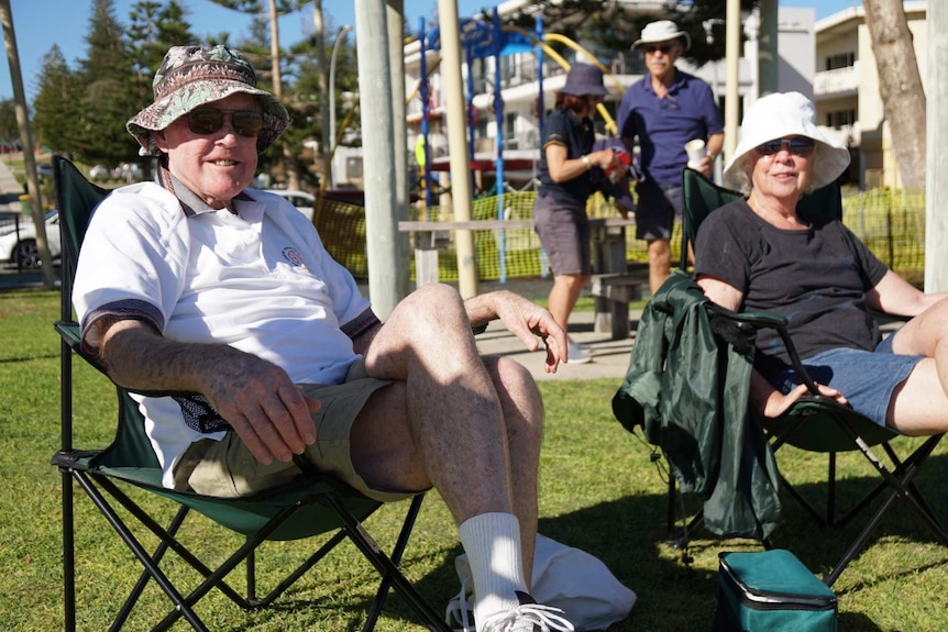 An elderly couple sit in a park enjoying the sunshine