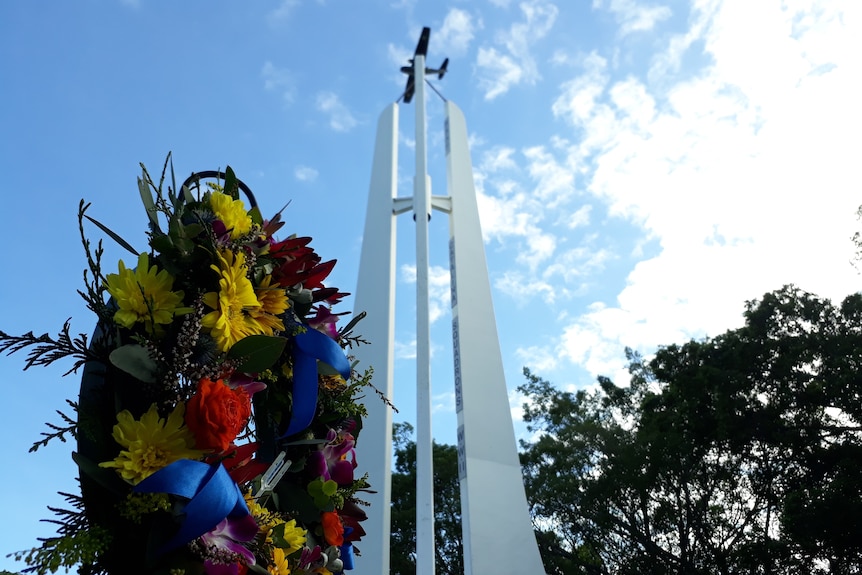 A large concrete structure with a small plane on top, with a flower-covered wreath infront