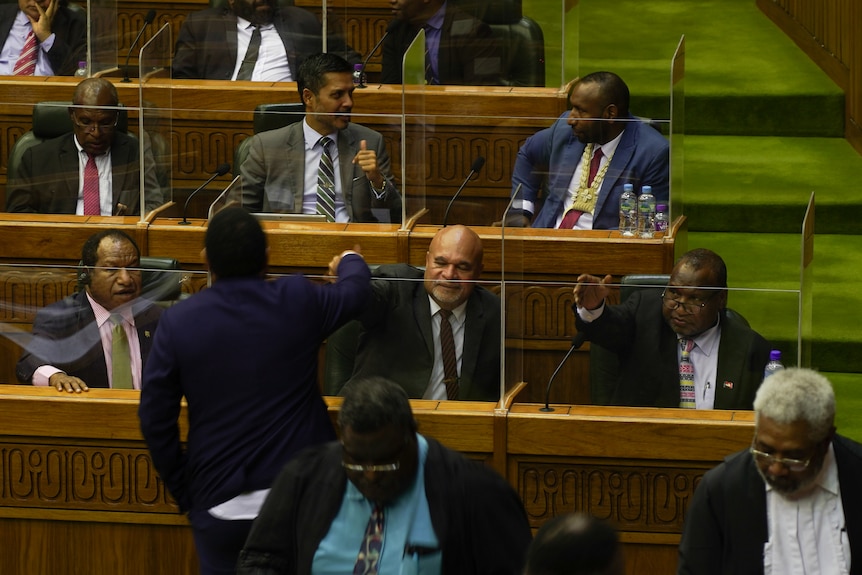 PNG politicians John Rosso and James Marape sit at their seats in a bright green carpeted chamber