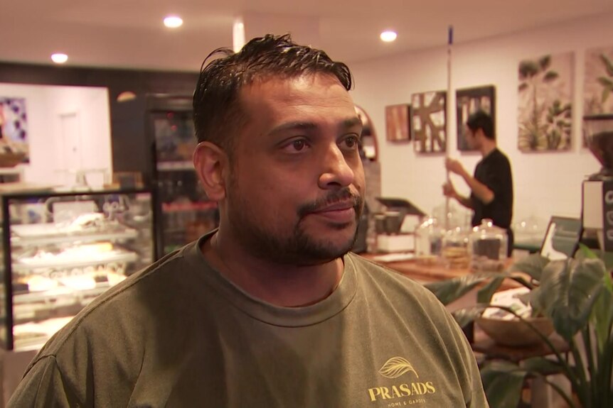 A man in a tshirt standing in a cafe.