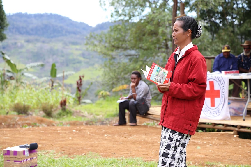 A woman stands holding a book and looking at a drama performance.