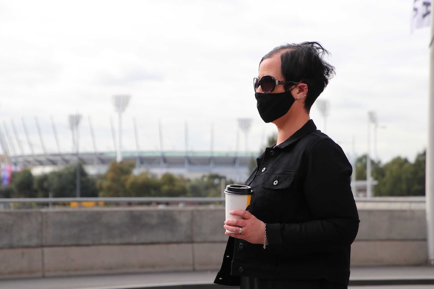 A woman in the CBD wears a face mask and sunglasses on a grey day. August 17, 2020