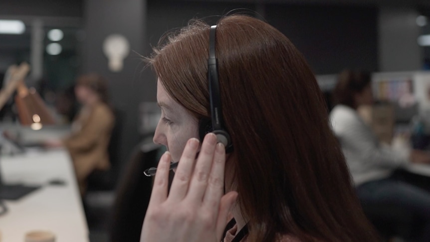 A woman with long hair wears a telephone headset.