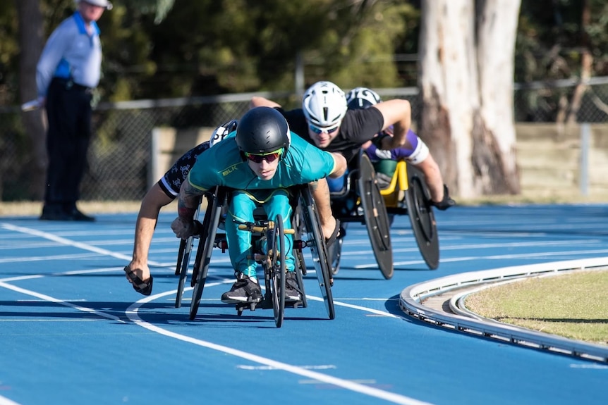 A trio of racers in wheelchairs speeding down an athletics track.