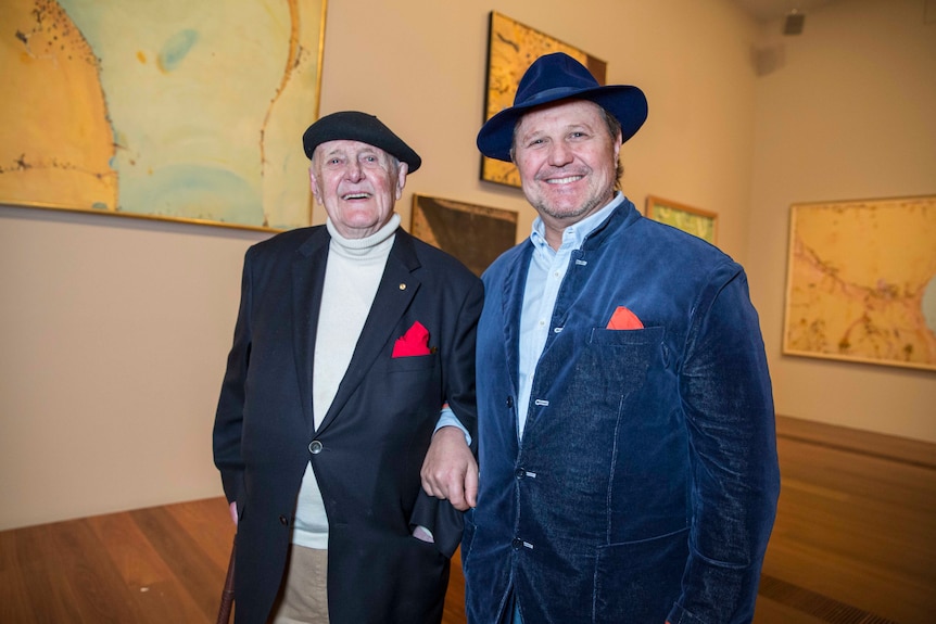 An elderly father and middle-aged son at an art gallery wearing jackets and matching red pocket squares.