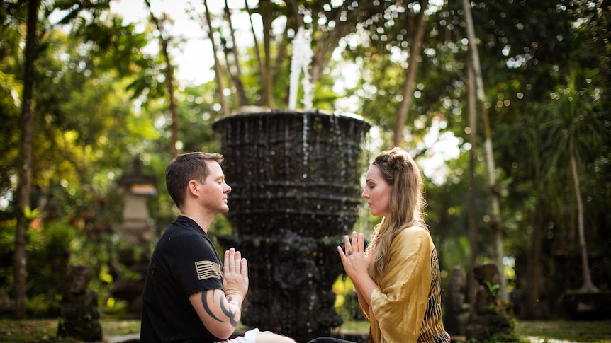 Photo of Autumn practicing yoga and meditation to treat her PTSD, she is sitting cross legged with a man, surrounded by trees.