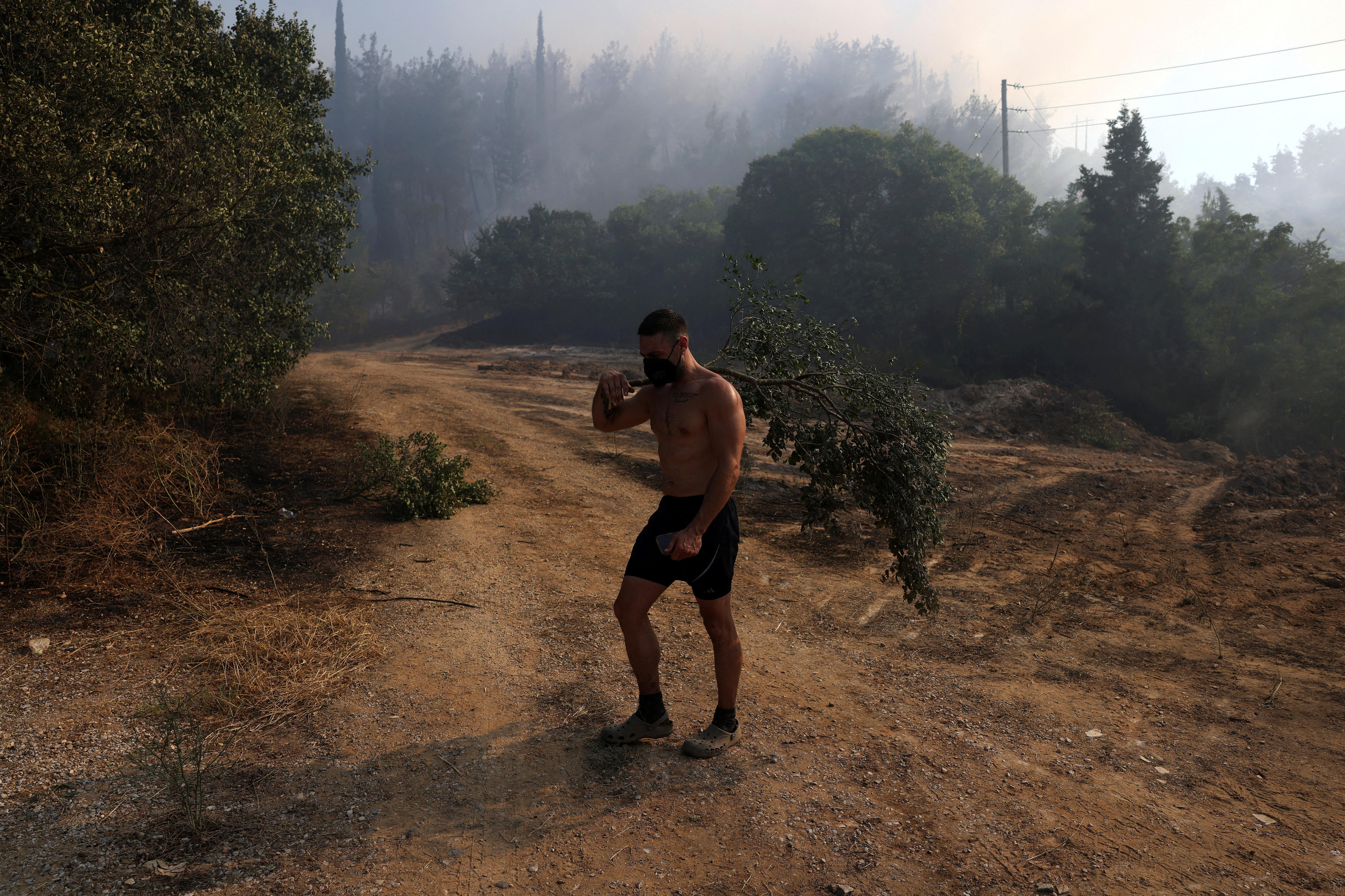 Un residente camina entre el humo que surge de un incendio forestal. Lleva pantalones cortos sin top y mascarilla.