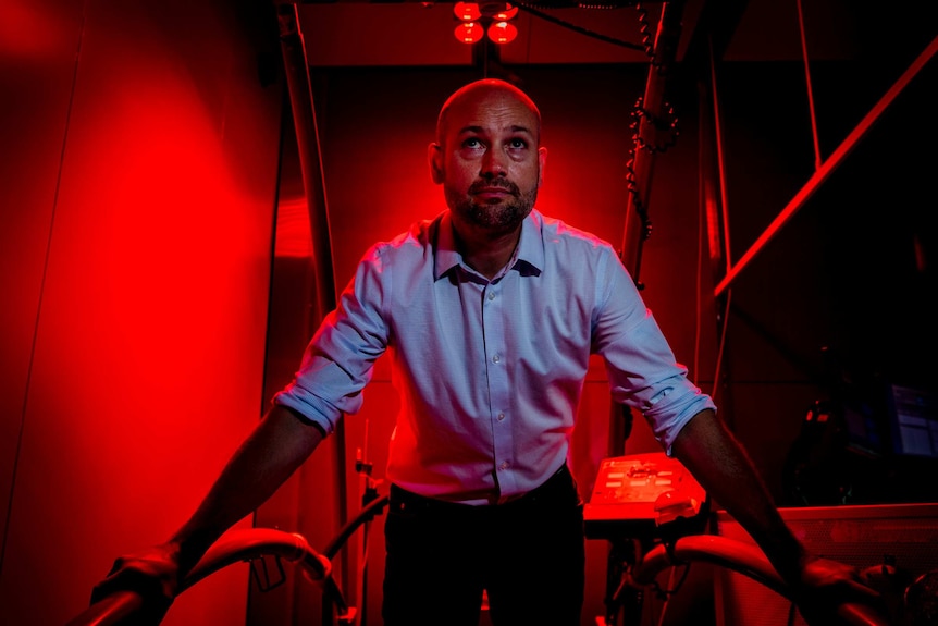 Man stands in lab under red heat lamps.