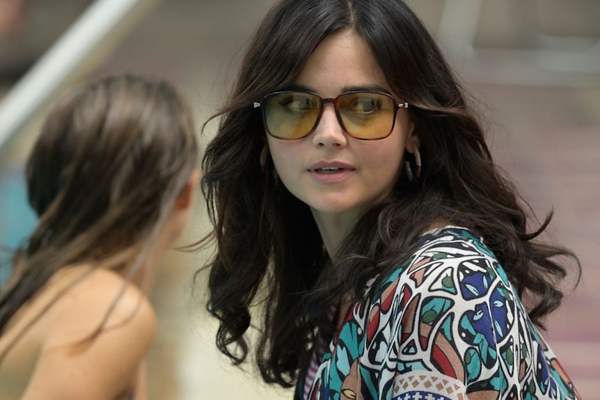 Jenna Coleman with 70s style hearing wearing yellow sunglasses.