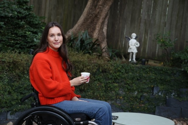 Young woman sits in a garden with a cup of coffee.