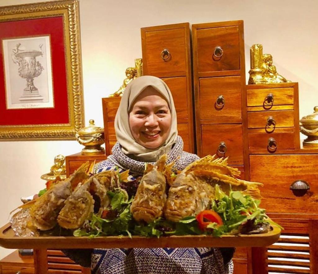 woman with head scarf holding wooden plate with fried fishes 