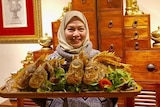 woman with head scarf holding wooden plate with fried fishes 