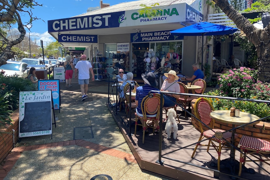 People walking along footpath and sitting in an out-door cafe.