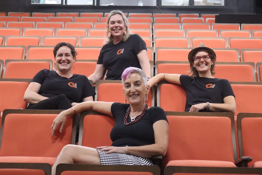 Four woman sit on new orange theatre seats, wearing black t-shirts and smiling.